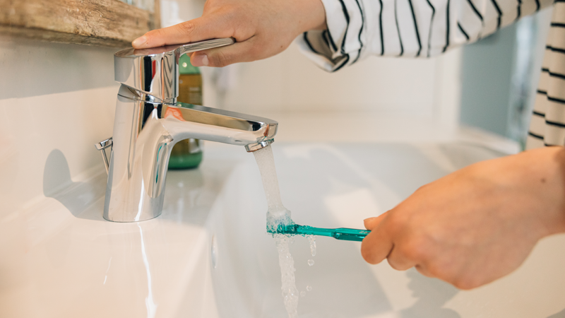 Person using a toothbrush under a running tap